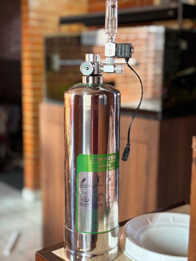 Sistema generador de CO2 por reacción química en tanque de acero inoxidable para acuario plantado, equipado con válvula solenoide de 12V, manómetro y contador de burbujas.